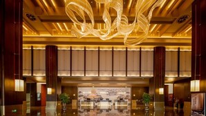 Eine großzügige Lobby mit spiegelndem Boden, einem imposanten Chandelier und einem Empfangsbereich mit Blick auf ein traditionelles Gebäude.