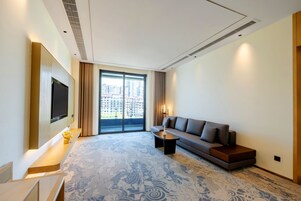 Una habitación de hotel moderna con un ventanal grande, un televisor de pantalla plana en la pared, un sofá, una mesita de centro y una alfombra estampada.