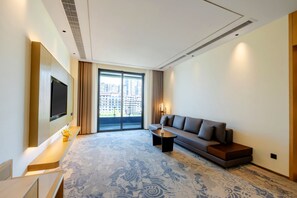 A modern hotel room with a large window, a flat-screen TV mounted on the wall, a sofa, a coffee table, and a patterned carpet. - Jingdezhen Grand Skylight Hotel (Jingdezhen)