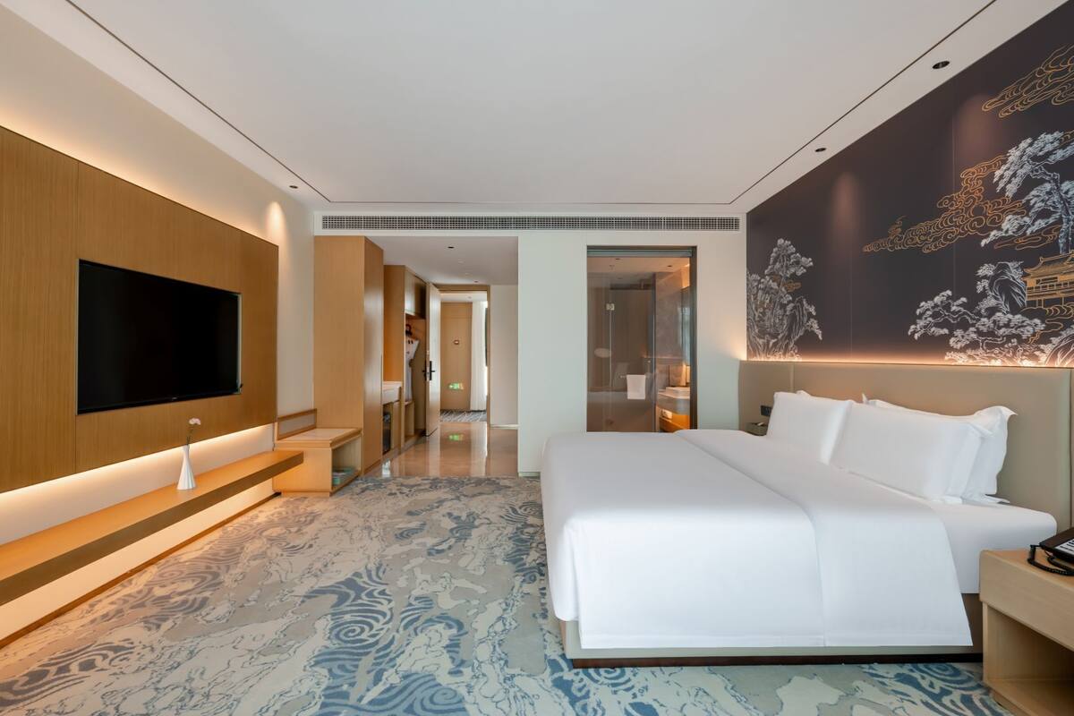 Una habitación de hotel moderna con una cama grande, un televisor de pantalla plana montado en la pared y un mural decorativo.