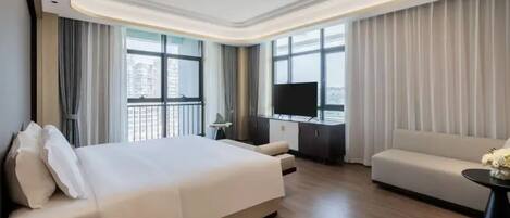 Ein modernes Hotelzimmer mit einem großen Bett, einer Couch, einem Fernseher und einem Balkon mit Vorhängen.