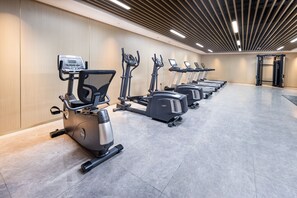 A row of stationary bikes and treadmills in a gym with a wooden wall and a ceiling with linear lights. - Jingdezhen Grand Skylight Hotel (Jingdezhen)