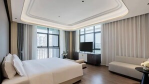 Ein modernes Hotelzimmer mit einem großen Bett, einer Couch, einem Fernseher und einem Balkon mit Vorhängen.