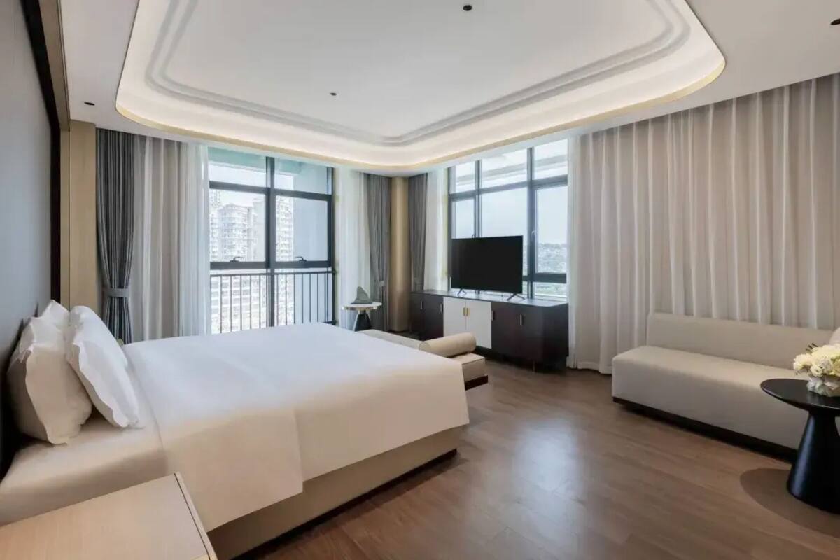 Una habitación de hotel moderna con una cama grande, un sofá, un televisor y un balcón con cortinas.