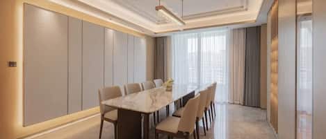 Uma sala de conferência moderna com uma mesa de mármore, cadeiras bege e uma grande janela com cortinas.