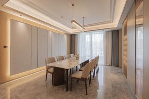 Una sala de conferencias moderna con una mesa de mármol, sillas color beige y un amplio ventanal con cortinas.