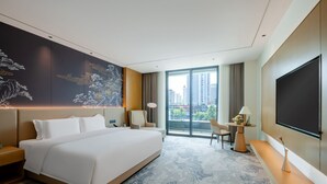 Ein modernes Hotelzimmer mit einem großen Bett, einem Schreibtisch mit Stuhl, einem Fernseher und Blick auf die Stadt.