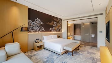 A modern hotel room with a large bed, bedside tables, a sofa, a decorative wall, and a bathroom visible through an open door.