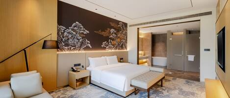 A modern hotel room with a large bed, bedside tables, a sofa, a decorative wall, and a bathroom visible through an open door.