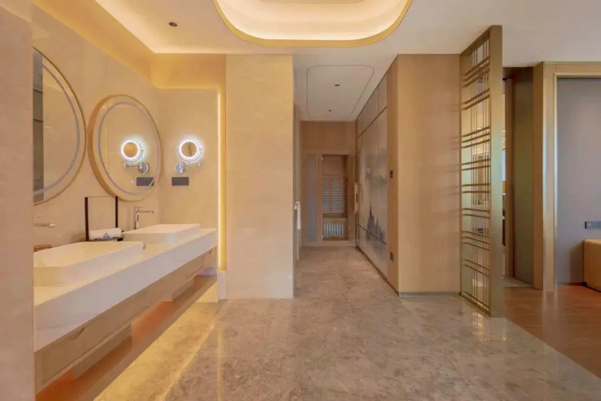 A modern bathroom with two sinks, illuminated mirrors, and a hallway leading to a room with a large window.