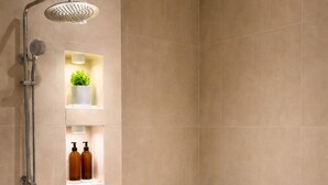 Un baño moderno con ducha, inodoro y estantes empotrados con artículos de aseo.