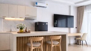 Una cocina moderna con una isla de madera, dos taburetes de bar, un televisor de pantalla plana y un ventilador de techo.