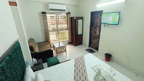 Ein Hotelzimmer mit Bett, Sessel, kleinem Tisch, Fernseher und einem Fenster mit Vorhängen.