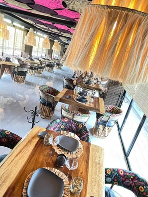 A restaurant with wooden tables and chairs, some with colorful upholstery. - Akuazul Resorts Adults Only Clothing Optional (Cancun)