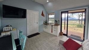 Een functioneel verblijf met kitchenette, eethoek, televisie aan de muur en een schuifpui naar buiten.