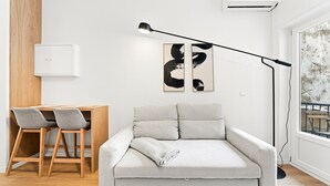 A modern living room with a grey sofa, wooden dining table with two chairs, a black floor lamp, and abstract art on the wall. - GuestReady - Comfort in the heart of Porto City (Porto)