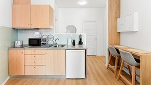 A compact kitchen with wooden cabinets, a white dishwasher, a microwave, and a coffee maker. There is a small dining area with a wooden table and two chairs. - GuestReady - Comfort in the heart of Porto City (Porto)