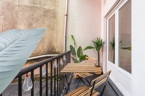 A balcony with a wooden table and chairs, potted plants, and hanging light bulbs. - GuestReady - Comfort in the heart of Porto City (Porto)