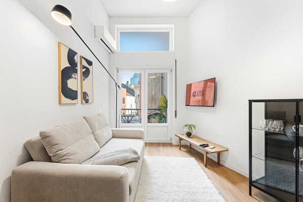 A modern living room with a sofa, a small table, a TV, and a glass cabinet. - GuestReady - Comfort in the heart of Porto City (Porto)