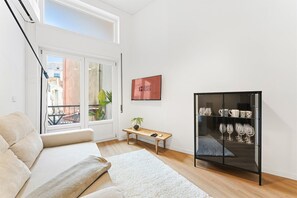 A modern living room with a sofa, a glass cabinet with wine glasses, a small table with a plant, and a framed picture on the wall. - GuestReady - Comfort in the heart of Porto City (Porto)