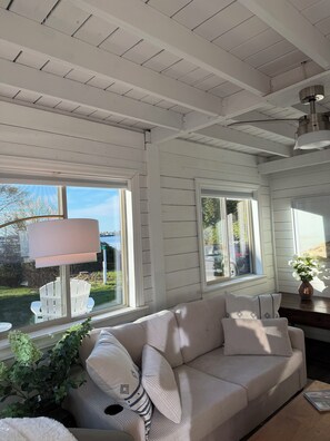 A room with a white wooden ceiling, large windows, a beige sofa, a lamp, and a plant. - 3-bedroom cottage in Harpswell with waterfront access to ash cove (Harpswell)