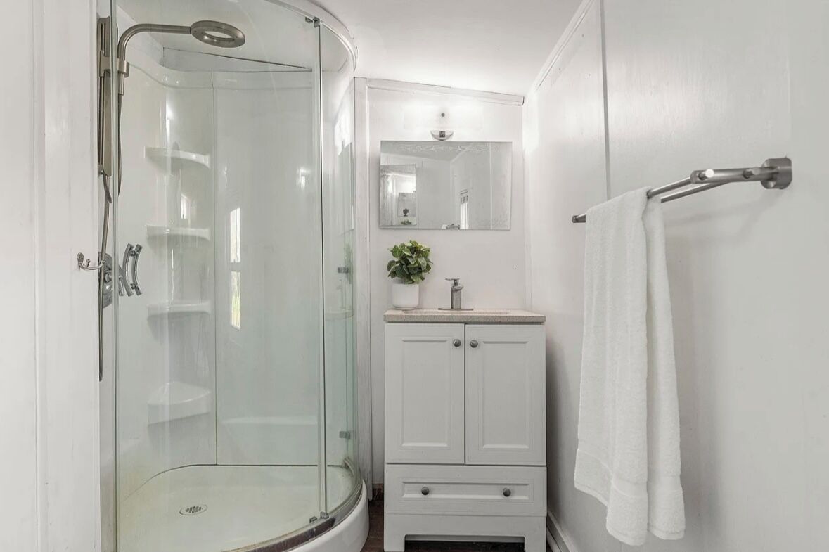 Un baño moderno con ducha envuelta en vidrio, tocador blanco con espejo y un perchero para toallas.