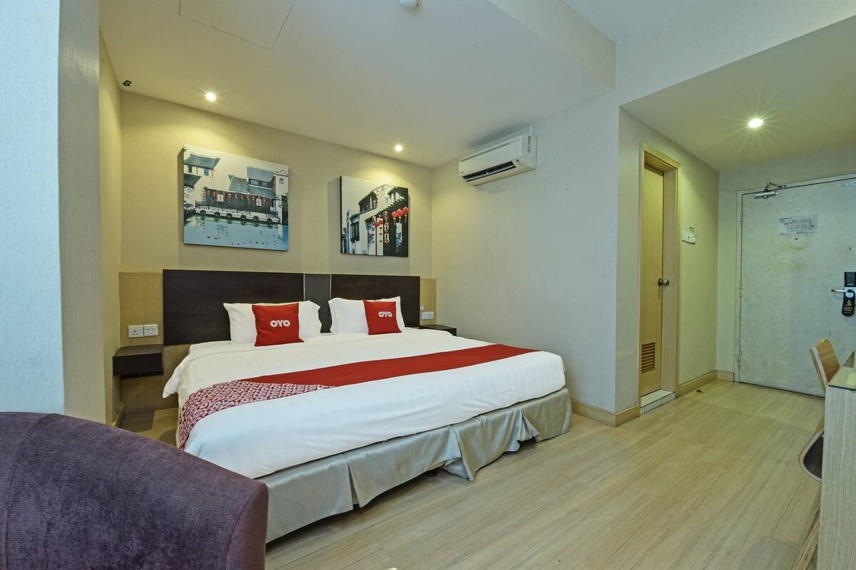 Quarto de hotel com uma cama grande, duas mesas de cabeceira, uma cadeira e uma porta que dá para um banheiro.