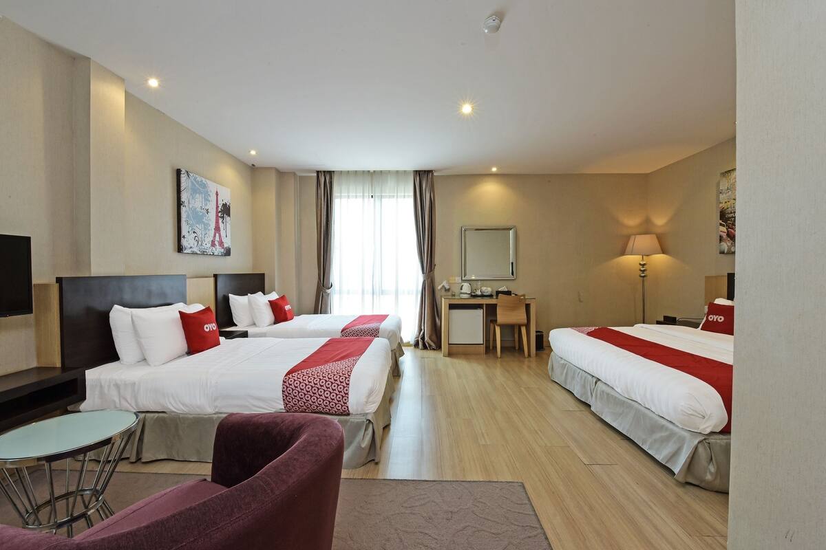 Quarto de hotel com duas camas, uma escrivaninha, uma cadeira e uma mesinha.