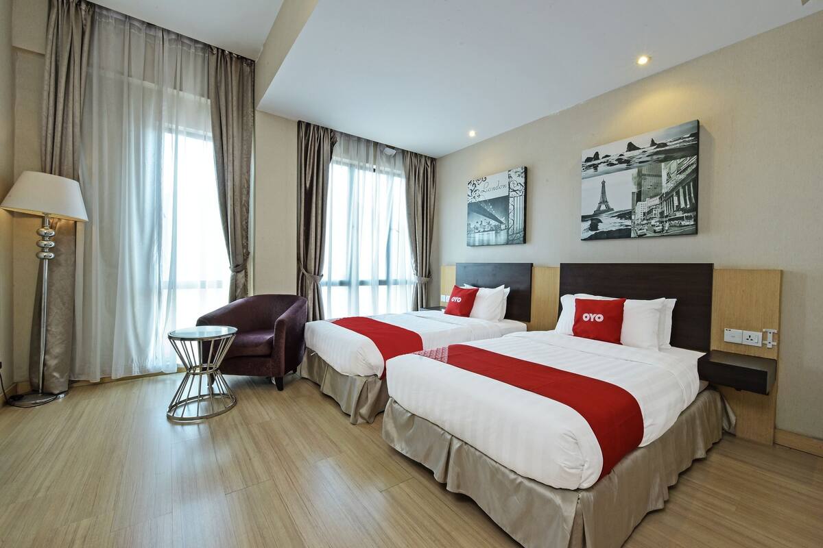 Quarto de hotel com duas camas, uma cadeira, um abajur e obras de arte na parede.