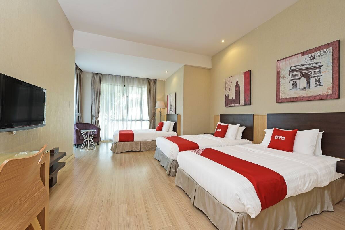 Quarto de hotel com duas camas, televisão, escrivaninha e área de refeições.