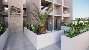 El exterior del Art Hotel Curacao, con un diseño moderno, presenta un pilar de piedra con el nombre del hotel, una palmera y diversas plantas en macetas.