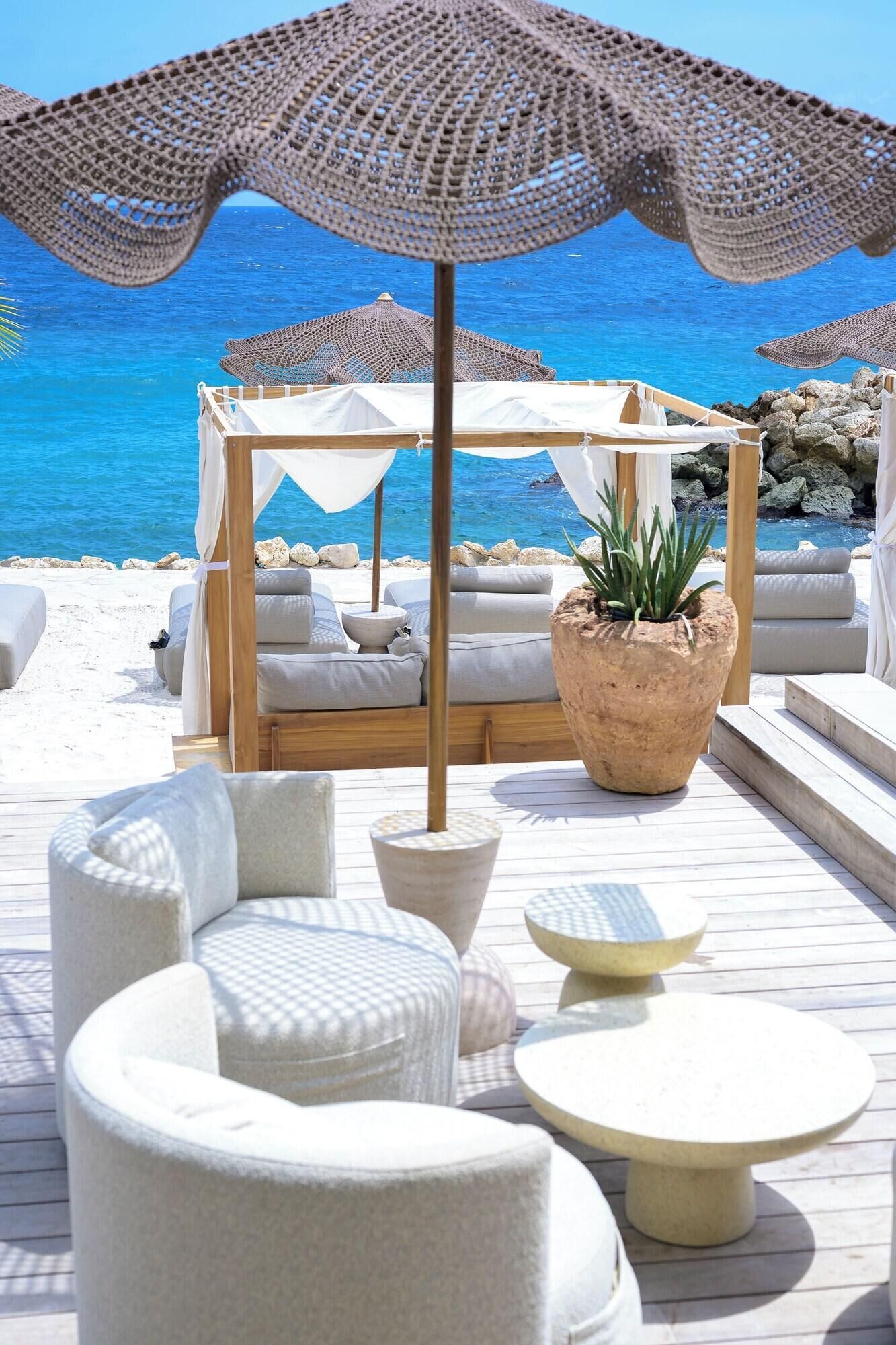 Un salon de plage avec des sièges en plein air, un grand parasol et un cabanon en bois.