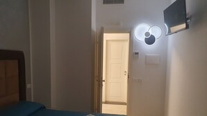 A hotel room with a bed, a flat-screen TV mounted on the wall, a door leading to another room, and a light fixture above the door. - Albergo Flaminia Rooms (Rome)