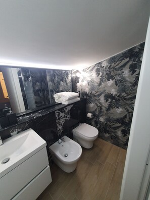 A compact bathroom with a black and white floral wallpaper, a white sink, a bidet, and a toilet. - Albergo Flaminia Rooms (Rome)