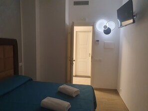 A hotel room with a bed, a flat-screen TV mounted on the wall, a door leading to another room, and a light fixture above the door. - Albergo Flaminia Rooms (Rome)