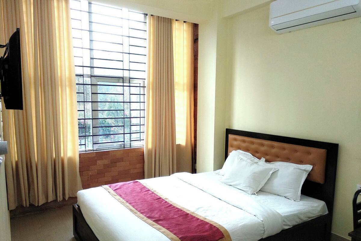 Una habitación de hotel con cama, cortinas, una ventana con vistas y un equipo de aire acondicionado.