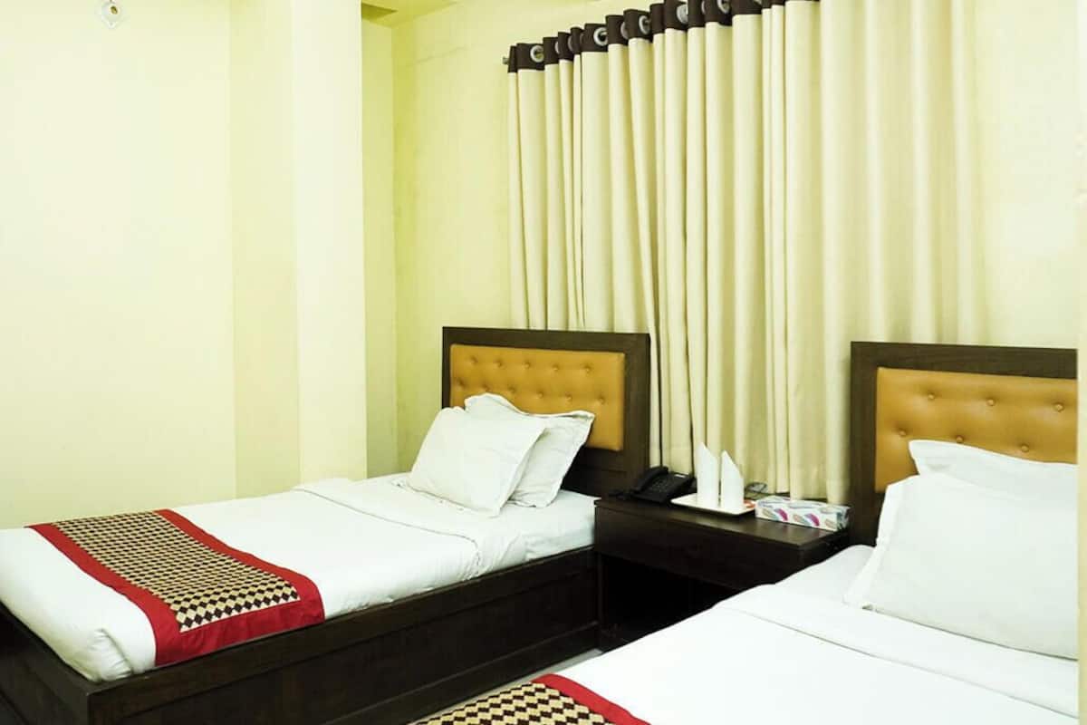Habitación de hotel con dos camas, una mesita de noche con teléfono y pañuelos, y una ventana con cortinas.