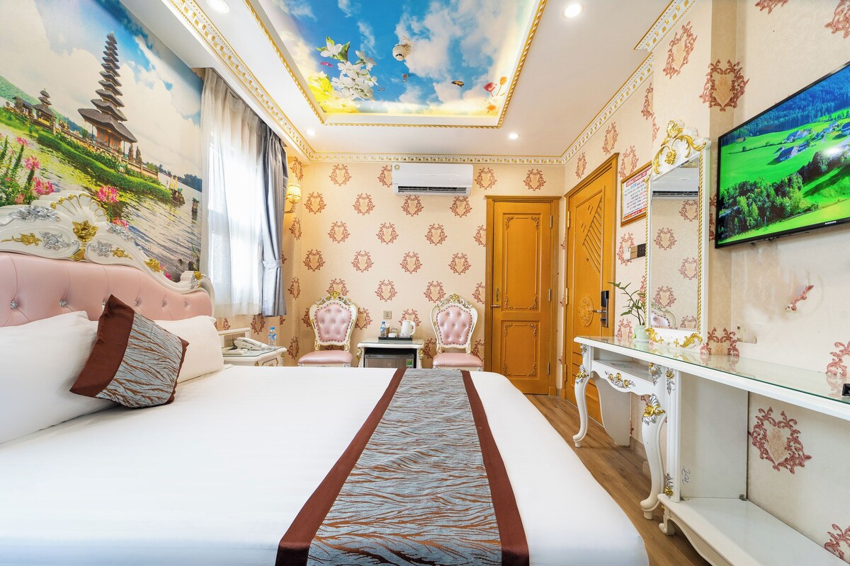 A hotel room with a large bed, a television, a desk, and a wardrobe.