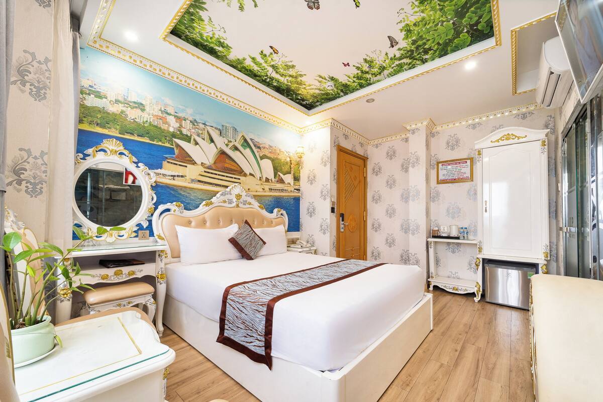 Une chambre d’hôtel avec un lit, une coiffeuse avec un miroir, une petite table et une plante en pot.