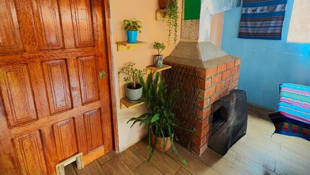 A room with a wooden door, a brick fireplace, and shelves with potted plants. - Enjoy a private room with breathtaking views of the Pisac mountains. (Pisac)