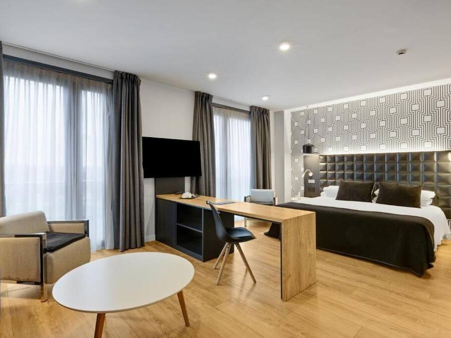 Una habitación de hotel moderna con cama, escritorio, silla, televisor y una pared con estampado.