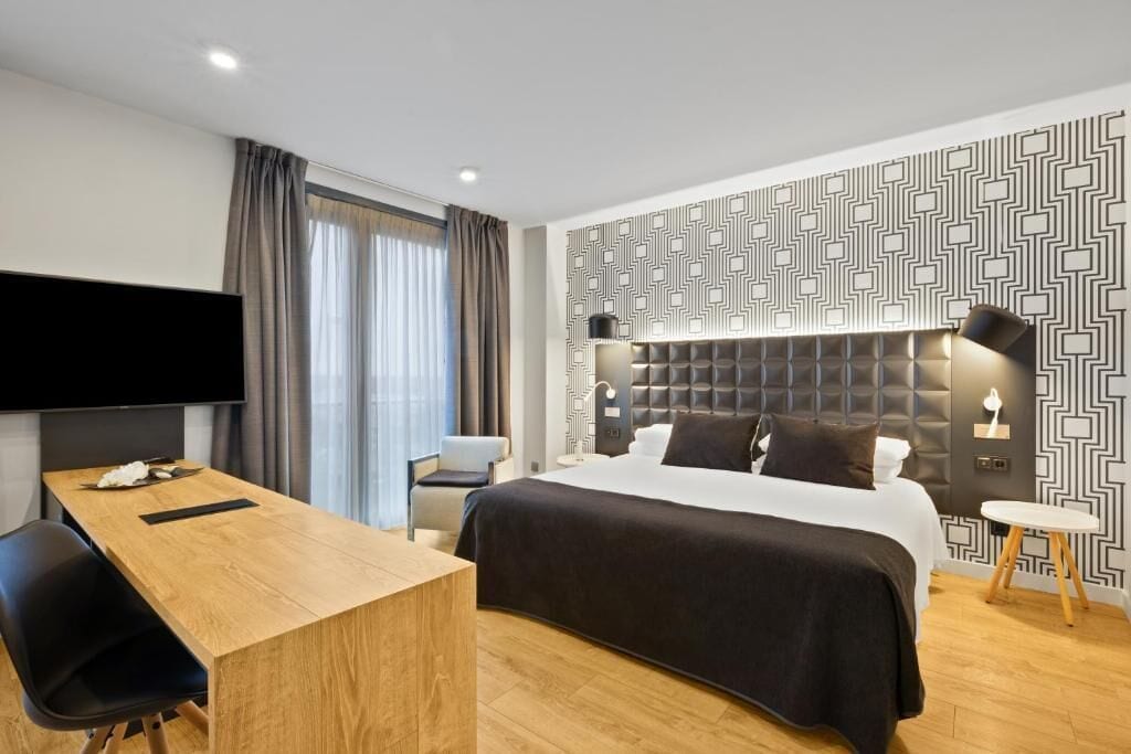 A modern hotel room with a large bed, a desk, a flat-screen TV, and a patterned wall.