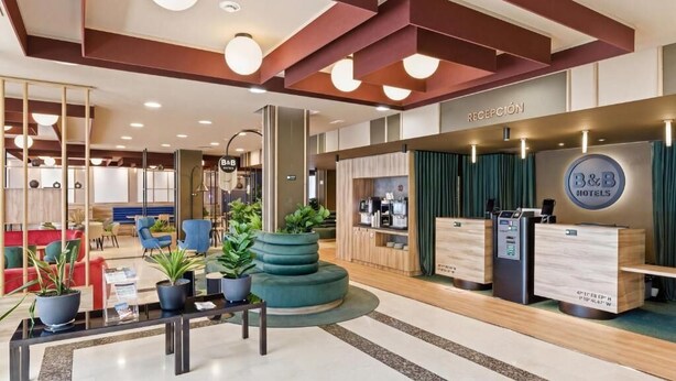 A hotel reception area with a reception desk, seating area, and a counter with a B&B logo. - B&b Hotel Tarragona Valls  (Alio)