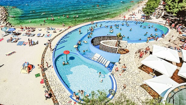 Ein Resort mit großzügigem Poolbereich, einem Strand und Meerblick.