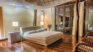 Une chambre d’hôtel avec un lit, des lampes de chevet, un ventilateur, un plancher en bois et une chaise en osier.