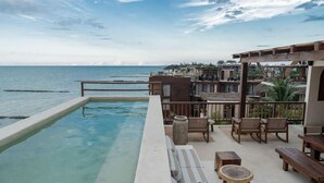 Un espace aménagé au bord de la piscine, avec vue sur la mer, comprenant des meubles en bois et un bac à fleurs en pierre.