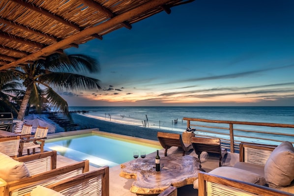 A beachside lounge with a pool, wooden furniture, and a view of the ocean at sunset. - Hotel Boutique Casa Muuch Holbox - Solo Adultos (Isla Holbox)