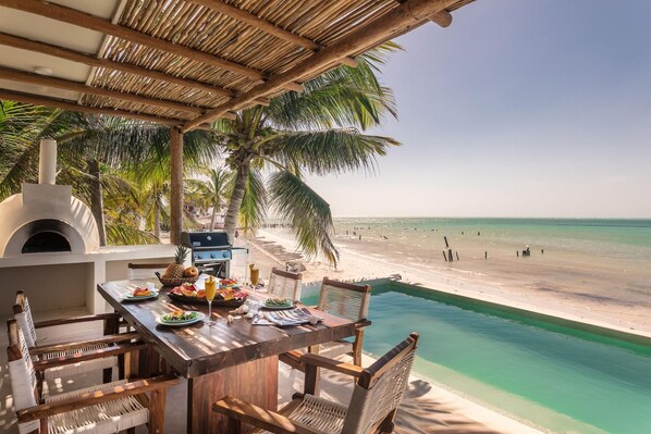 Un espace de restauration situé au bord de la plage, avec une piscine, un barbecue et une vue sur la plage.