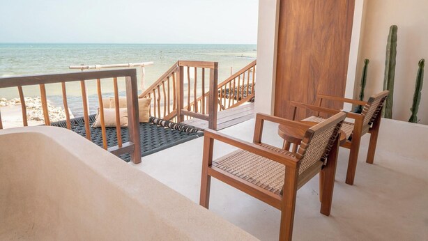 Un balcon avec vue sur la mer, des chaises en bois et une porte en bois.