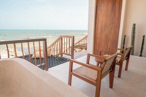 Un balcón con vista al mar, sillas y puerta de madera.